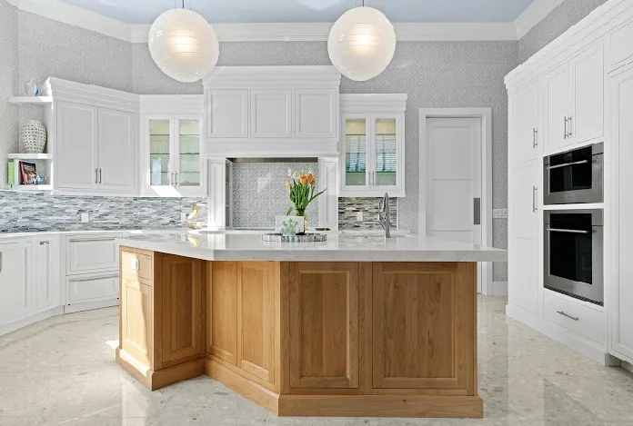 White kitchen with wood island, marble countertops, and pendant lighting.