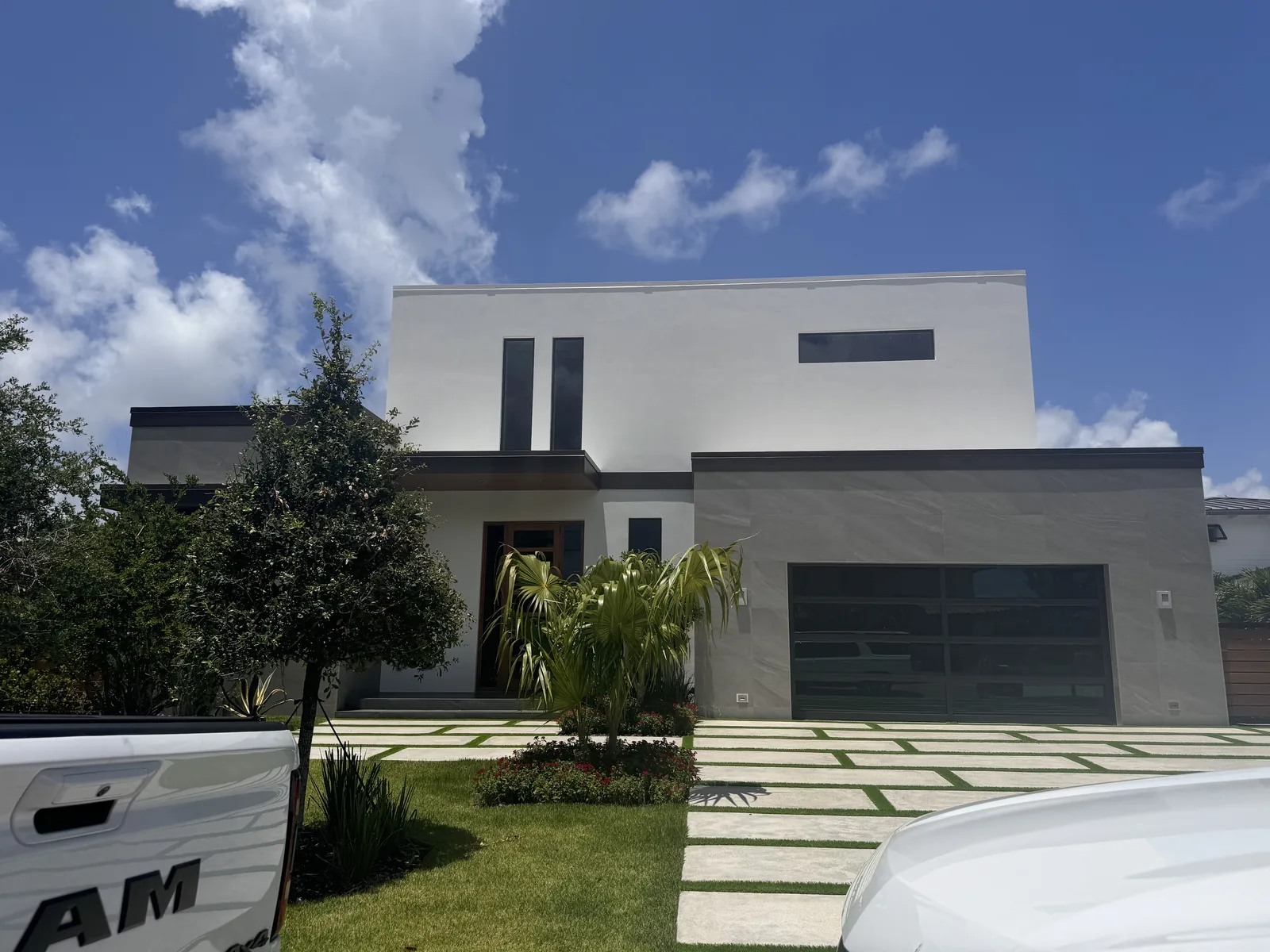 White and gray residential home with geometric hardscape and tropical landscaping.