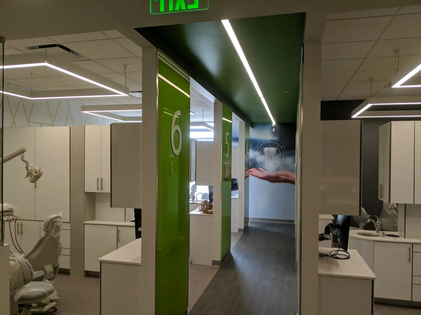 Dental operatory with cream cabinetry, green accent walls, linear ceiling lights.