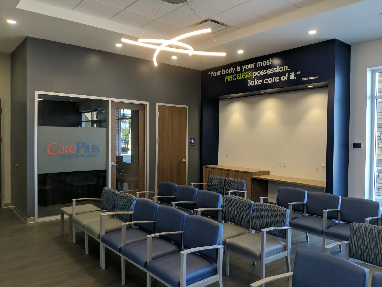 Medical waiting room with wellness-themed wall graphics and blue-gray seating.