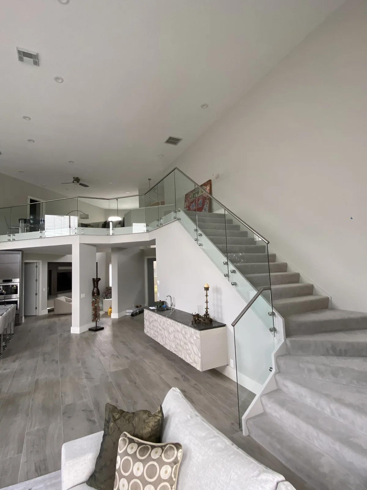 Open-concept interior with floating staircase, glass railing, luxury kitchen beyond.