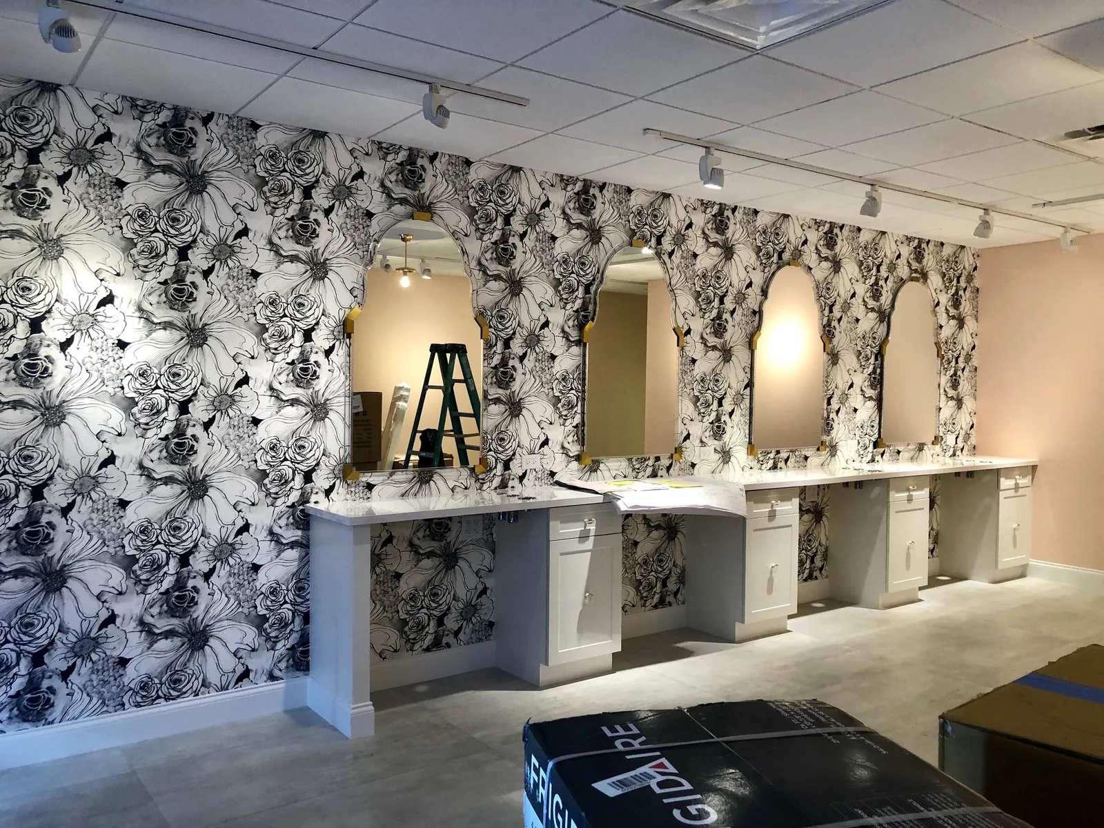 Vanity area with floral wallpaper, multiple mirrors, pendant lighting.