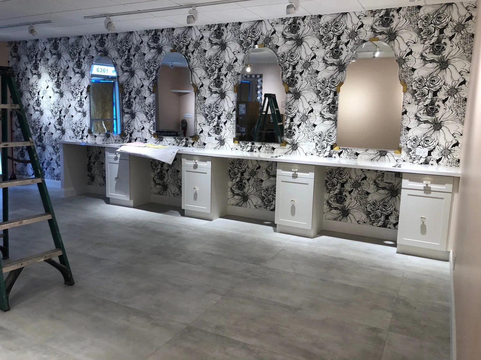 Bathroom vanity with white cabinetry, floral wallpaper, illuminated mirrors.