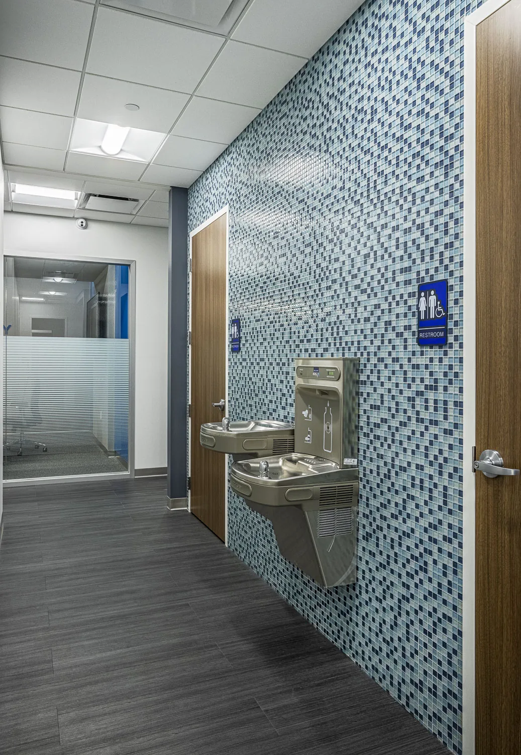 Commercial restroom with blue mosaic tile, drinking fountains, accessible fixtures.