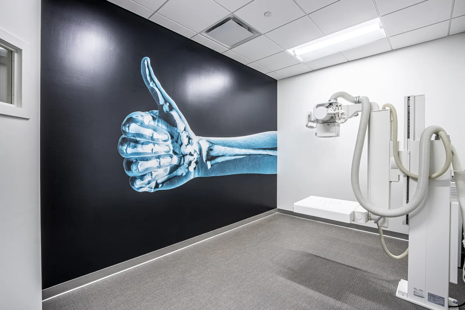X-ray room with thumbs-up radiograph on dark accent wall and diagnostic equipment.