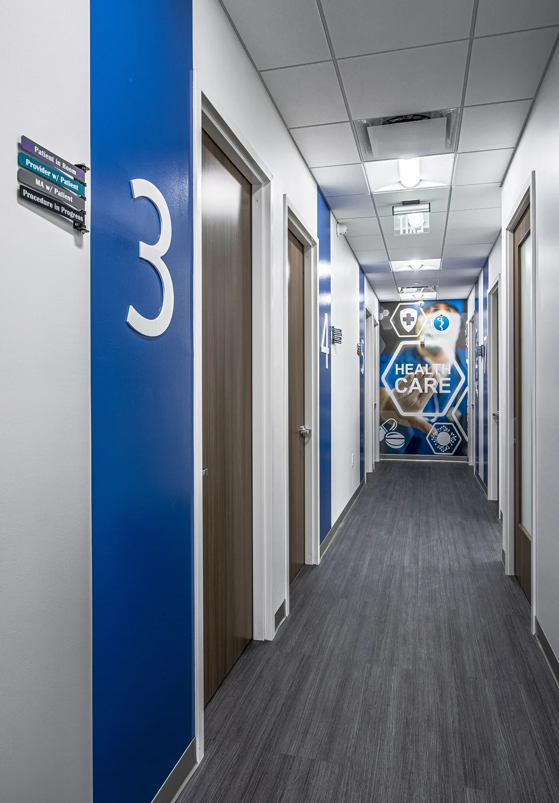 Medical office hallway with blue accent wall and numbered treatment room signage.