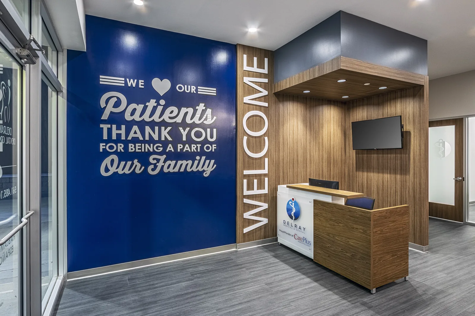 Medical clinic reception with blue welcome wall and front desk.
